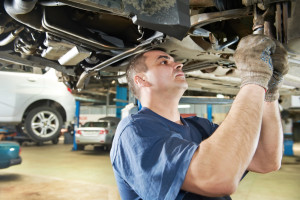 Car mechanic examining car suspension of lifted automobile at repair service station